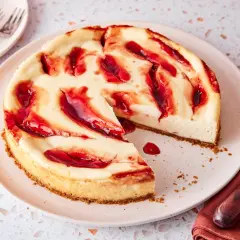 Ein cremiger american cheesecake mit roten Fruchtsaucen-Wirbeln auf einem Teller, bereit zum Genießen.