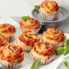 Leckere Pizza Muffins mit Salami und Käse, garniert mit frischem Basilikum.