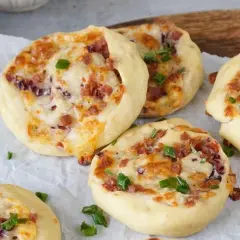 Flammkuchen Schnecken mit Speck, Käse und Frühlingszwiebeln, gebacken auf Backpapier.