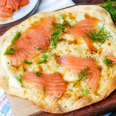 Flammkuchen mit Lachs, belegt mit zarten Lachsscheiben, geschmolzenem Käse und frischem Dill, garniert mit Pfeffer.