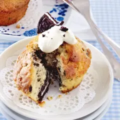 Ein aufgeschnittener Oreo Muffin mit Sahne und einem Oreo-Stück obendrauf, serviert auf einem Spitzendeckchen.