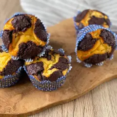 Schokoladen-Vanille-Zupfkuchen-Muffins in blauen Papierförmchen auf einem Holzbrett.