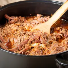Zartes pulled pork im Dutch Oven, bereit zum Servieren. Ein Holzlöffel liegt darin.