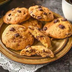 Saftige american cookies mit Schokoladenstückchen auf einem Teller, daneben eine Tasse Kaffee.