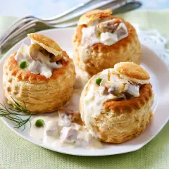 Drei Blätterteig-Schiffchen gefüllt mit cremigem Ragout Fin, garniert mit Erbsen und Dill.