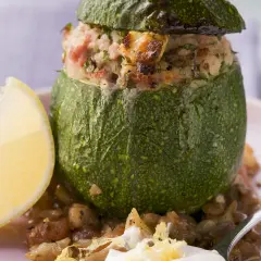 Gefüllte, runde Zucchini mit einer herzhaften Mischung aus Reis und Fleisch, serviert mit einer Zitronenspalte und Linsen.