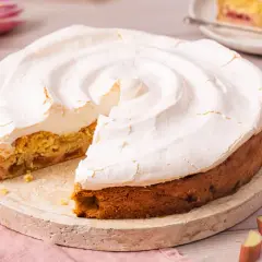 Ein köstlicher Rhabarberkuchen mit Baiser, dessen fluffige Haube leicht gebräunt ist. Ein Stück fehlt bereits.