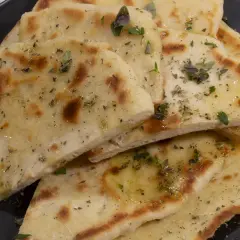 Griechisches Fladenbrot mit Trockenhefe, bestreut mit Kräutern und Olivenöl, auf einem schwarzen Teller.