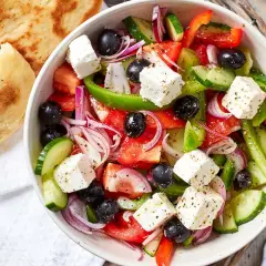 Frischer griechischer Salat mit Tomaten, Gurken, roten Zwiebeln, Oliven und Feta-Käse, serviert mit Fladenbrot.