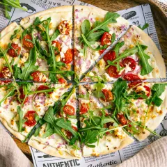 Ein köstlicher flammkuchen vegetarisch mit Kirschtomaten, Rucola und Ziegenkäse auf dünnem Teig.
