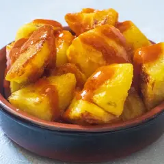 Knusprige Kartoffelstücke, überzogen mit einer würzigen Sauce, serviert als köstliche Patatas Bravas in einer kleinen Schale.