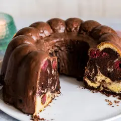 Ein saftiger Marmorkuchen mit Kirschen, überzogen mit Schokoladenglasur, auf einem weißen Teller.