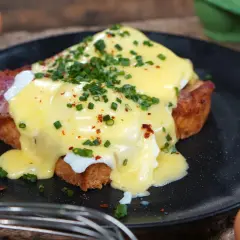 Ein köstliches Egg Benedict mit pochiertem Ei, Speck und Sauce Hollandaise, garniert mit Schnittlauch und Chiliflocken.