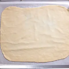 Dünn ausgerollter Flammkuchenteig liegt auf einem Backblech, bereit für leckere Beläge.