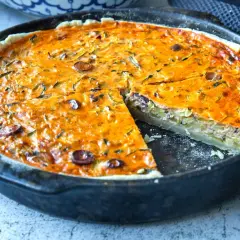 Eine köstliche Zucchini-Quiche mit Oliven in einer Gusseisenpfanne, eine Scheibe herausgeschnitten.