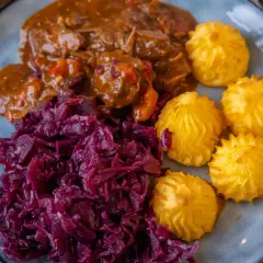 Herzoginkartoffeln selber machen ist einfach! Hier sind sie mit deftigem Gulasch und Rotkohl auf einem Teller angerichtet.