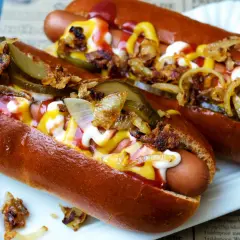 Zwei appetitliche Hot Dogs mit Senf, Ketchup, Mayonnaise, Gurken und Röstzwiebeln.