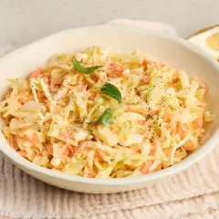 Cremiger Coleslaw Salat mit Karotten und Kohl, garniert mit Petersilie und Pfeffer. Dazu Zitronenspalten.