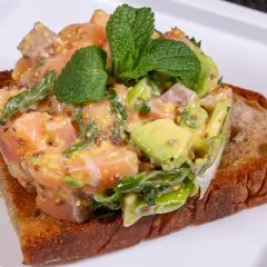 Lachs-Tatar mit Avocado auf geröstetem Brot, garniert mit Minze. Ein Gericht, das selbst Sterneköche begeistert.