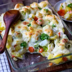 Herzhafter vegetarischer Auflauf mit Kartoffeln, Brokkoli, Blumenkohl und Karotten, überbacken mit Käse. Ein Holzlöffel liegt bereit.
