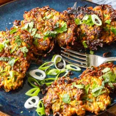 Knusprige zucchini pfannkuchen, garniert mit frischen Kräutern und Frühlingszwiebeln, liegen auf einem blauen Teller. Eine Gabel liegt daneben.