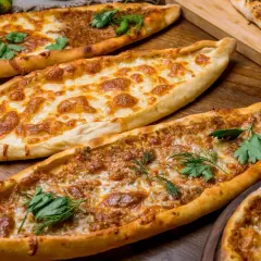 Mehrere Pide-Gerichte, darunter eines mit Käse und eines mit Hackfleisch, sind auf einem Holztisch angerichtet. Ein köstliches Pide Rezept!