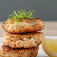 Gestapelte Fischbuletten, garniert mit Dill, neben einer Zitronenspalte. Ein leckeres Buletten Rezept.