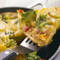 Ein Stück herzhaftes Omelett mit Brokkoli, Kartoffeln und Schinken wird aus einer Pfanne gehoben. Ein tolles Omelett Rezept für jeden Tag.