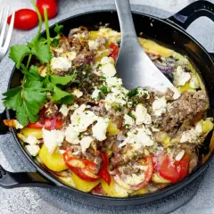 Herzhaft gebackener Feta mit Hackfleisch, Kartoffeln und Tomaten in einer schwarzen Gusseisenpfanne, garniert mit frischer Petersilie.