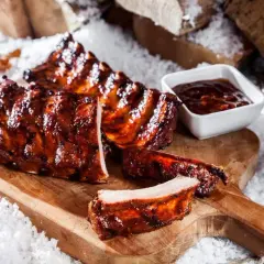 Saftige spareribs im backofen, glasiert und mit BBQ-Sauce, auf einem Holzbrett im Schnee.