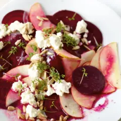 Rote Bete Salat mit Apfel, zerbröckeltem Käse und Sonnenblumenkernen auf einem weißen Teller.