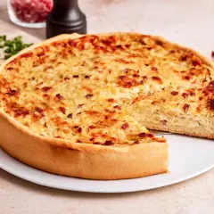 Ein goldbrauner Zwiebelkuchen mit Speck, ein Stück herausgeschnitten. Perfekt für ein Zwiebelkuchen Rezept.