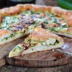 Eine köstliche Zucchini-Pizza mit goldbraunem Teig und saftiger Füllung, auf einem rustikalen Holzbrett serviert.