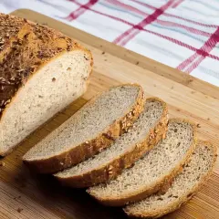 Ein frisch gebackenes Brot, perfekt für ein keto brot rezept, liegt auf einem Holzbrett. Mehrere Scheiben sind bereits abgeschnitten.