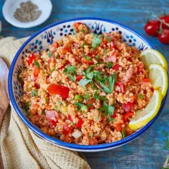 Frischer Bulgur Salat mit Tomaten, Paprika und Kräutern, garniert mit Zitronenspalten. Ein leichter Genuss!