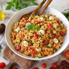 Ein bunter Risoni Salat mit Kirschtomaten, Mozzarella-Kugeln und Gurken, garniert mit frischem Basilikum.