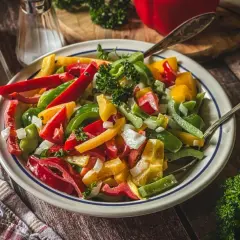 Bunter Paprika Salat mit Zwiebeln und Petersilie, serviert auf einem Teller mit zwei Löffeln.