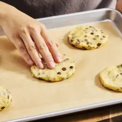Hände formen Teig für Chocolate Chip Cookies auf einem Backblech. Der Teig ist voller Schokoladenstückchen, bereit für den cookie crumble.