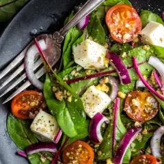 Frischer mangold salat mit Kirschtomaten, roter Zwiebel und Feta-Käse, garniert mit Nüssen und einem Dressing.