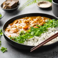 Ein Teller mit dampfendem japanischem Curry, Reis, Frühlingszwiebeln und Petersilie. Daneben kleine Schalen mit Currywürfeln und Gewürzen.