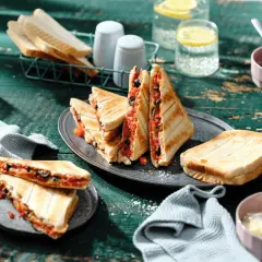 Leckere Sandwichmaker Rezepte: Getoastete Sandwiches mit Tomaten und Oliven, serviert mit Zitrone-Wasser.
