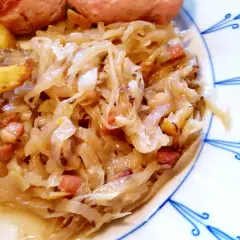 Herzhaftes bayrisch Kraut mit Speckwürfeln, serviert mit knusprigen Kartoffelspalten und einer Wurst. Ein Klassiker!