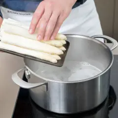 Frischer weißer Spargel wird in kochendes Wasser gegeben. So beginnt das Spargel kochen mit oder ohne Deckel.