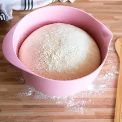Hefeteig für einen Blechkuchen ruht in einer rosa Schüssel. Daneben liegt ein Holzlöffel mit Herz.