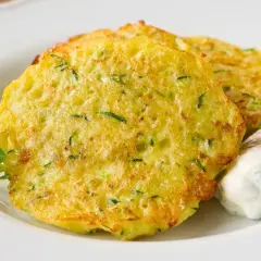 Goldbraune Zucchini-Puffer mit Kräuterquark und frischem Grün.