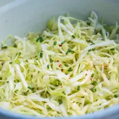 Frischer Spitzkohl Salat, fein geschnitten und mit Schnittlauch und Chiliflocken garniert, wartet in einer Schüssel.