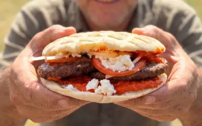 Ein Mann hält eine saftige Pljeskavica mit Tomaten, Zwiebeln und Käse. Ein tolles Rezept für den Sommer!