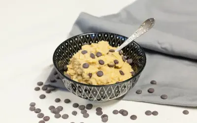 Schüssel mit essbarem Keksteig und Schokostückchen, daneben verstreute Schokotropfen. Ein Löffel steckt im Teig.