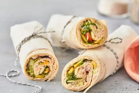 Drei leckere Thunfisch-Wraps, gefüllt mit Salat, Gurke und Tomate, sind in Papier gewickelt und mit Schnur verschnürt.