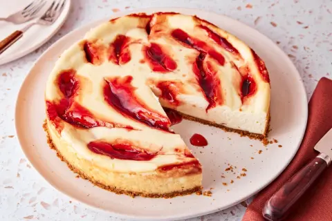 Ein cremiger american cheesecake mit roten Fruchtsaucen-Wirbeln auf einem Teller, bereit zum Genießen.